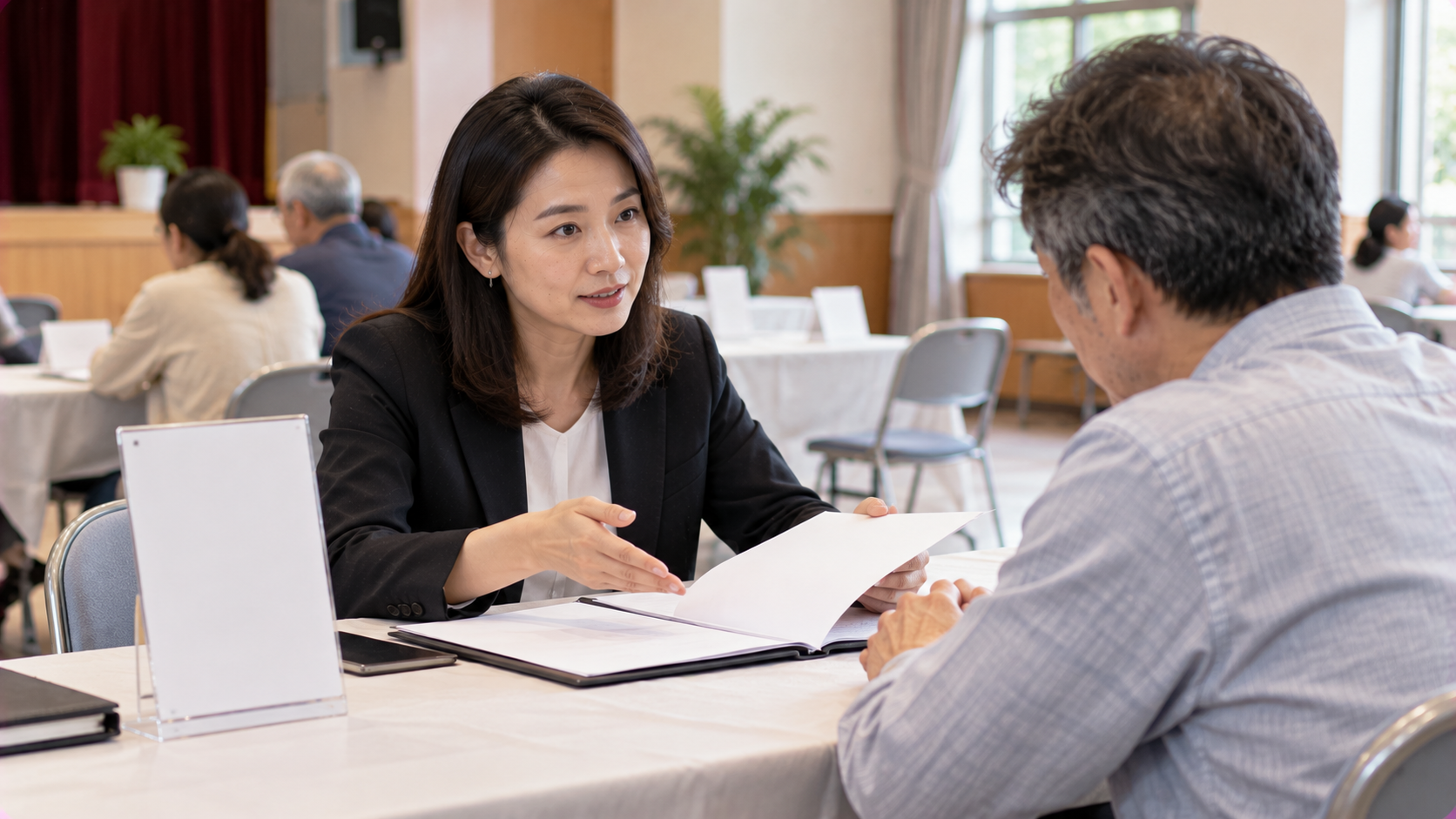 亞洲女性律師在社區法律諮詢攤位向亞洲中年男性說明債務更生與法律扶助程序